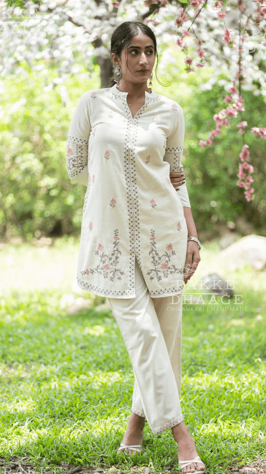 Woman in a white printed co-ord set with minimalistic prints standing in a garden with greenery and flowers.