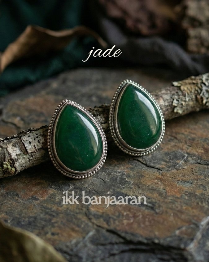 Jade earrings with art-silver settings on a stone surface, featuring the brand 'ikk banjaaran'.