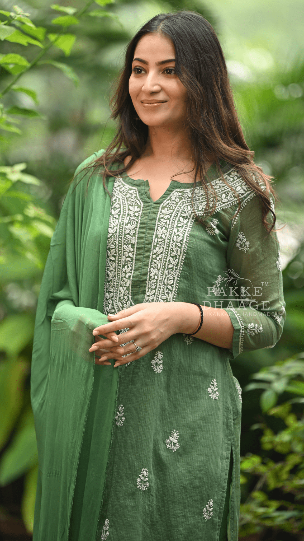 Woman wearing a green traditional chikankari outfit with embroidery, standing against a blurred natural background.