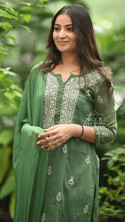 Woman wearing a green traditional chikankari outfit with embroidery, standing against a blurred natural background.