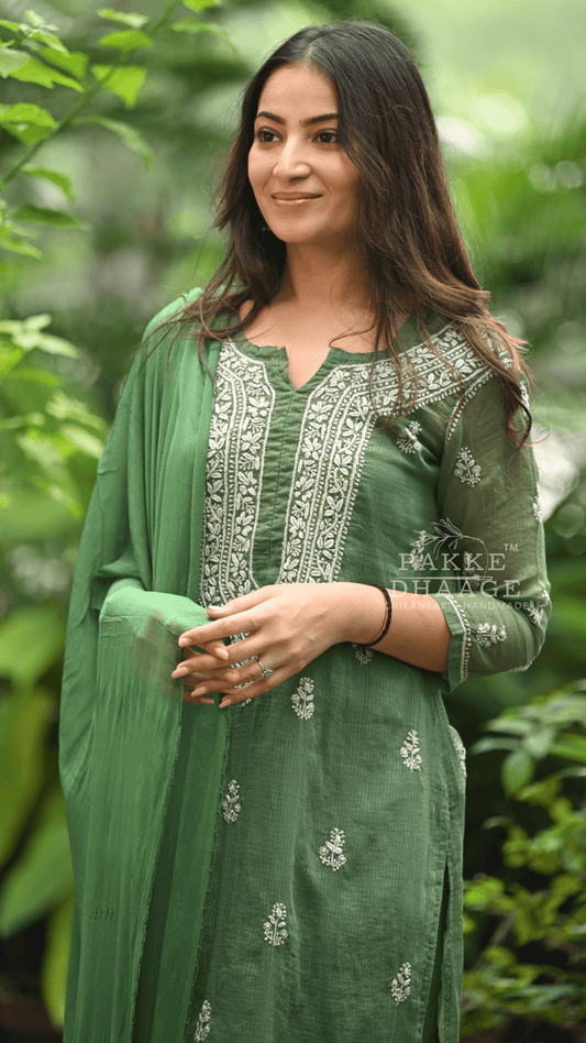 Woman wearing a green traditional chikankari outfit with embroidery, standing against a blurred natural background.