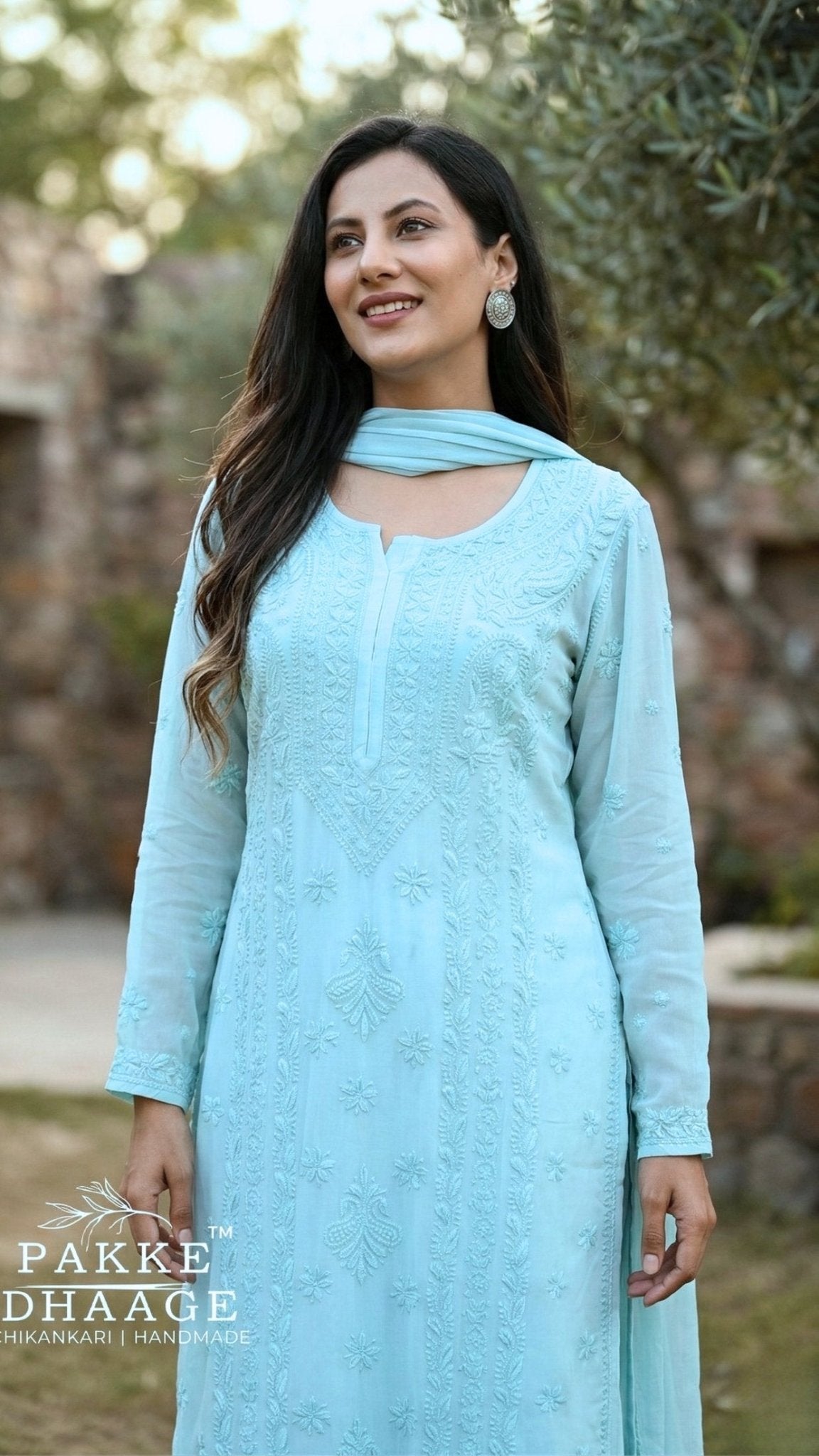 Woman wearing a light blue elegant chikankari outfit with a dupatta, standing outdoors.