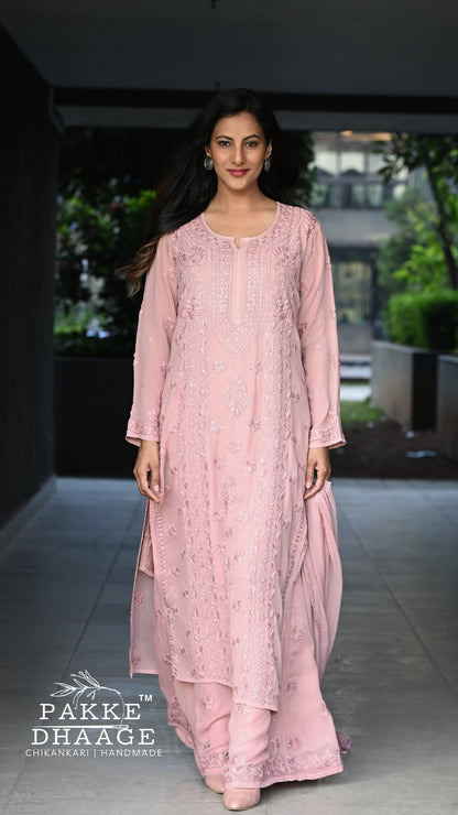 Woman wearing a pink traditional chikankari outfit with intricate designs, standing in an outdoor setting.