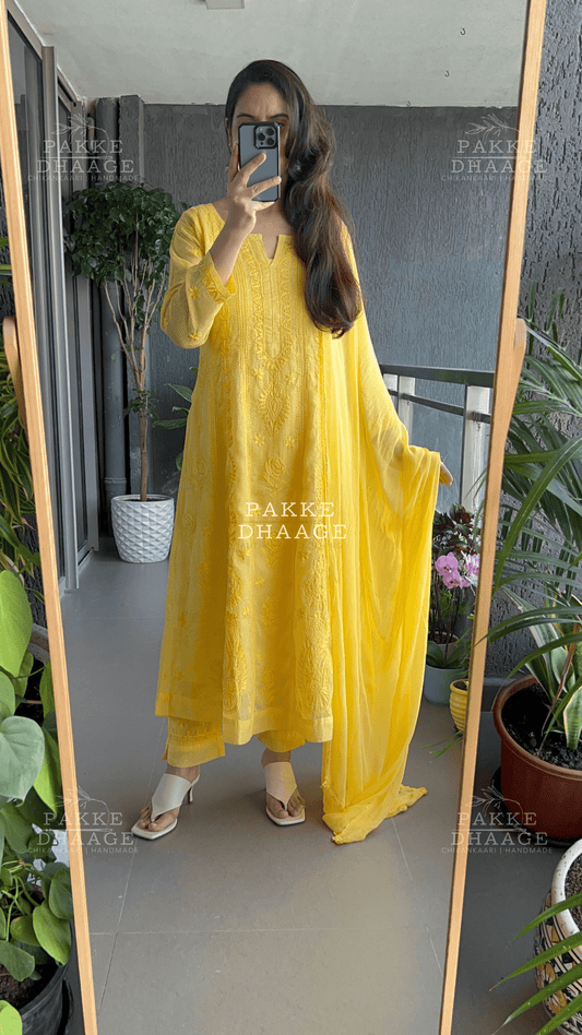 woman wearing a yellow chikankari set standing in front of a mirror with plants around.
