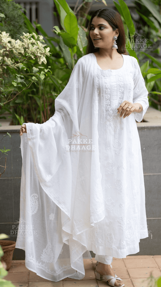 Woman wearing a white chikankari anarkali suit with a flowing drape in an outdoor setting.