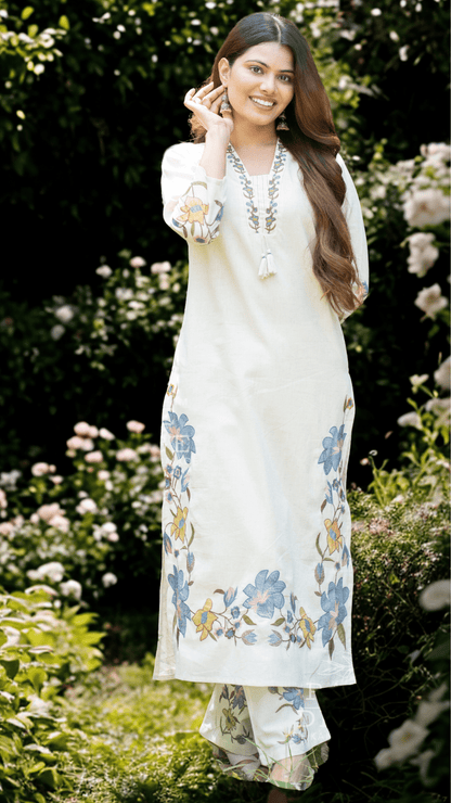 Woman in a white printed suit set standing in a garden with flowers.