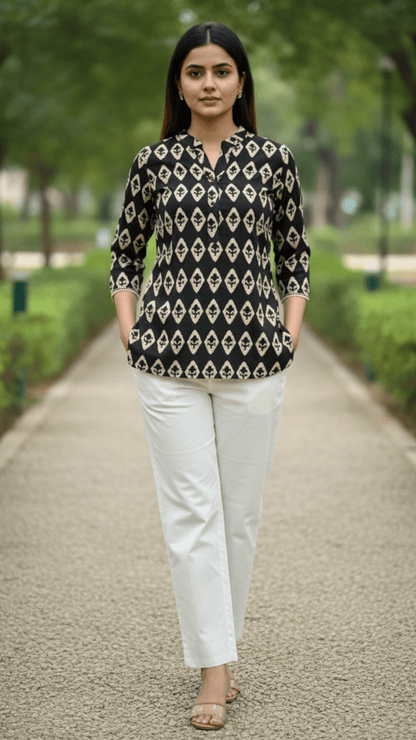 Woman wearing a black and white patterned top and white pants walking on a path with greenery in the background